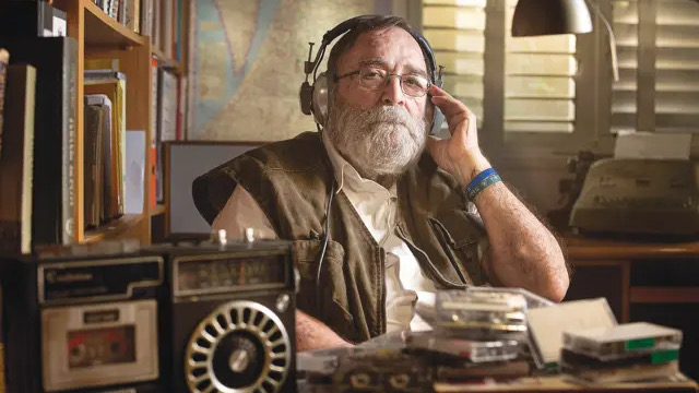 A bearded man with headphones on sitting at a desk