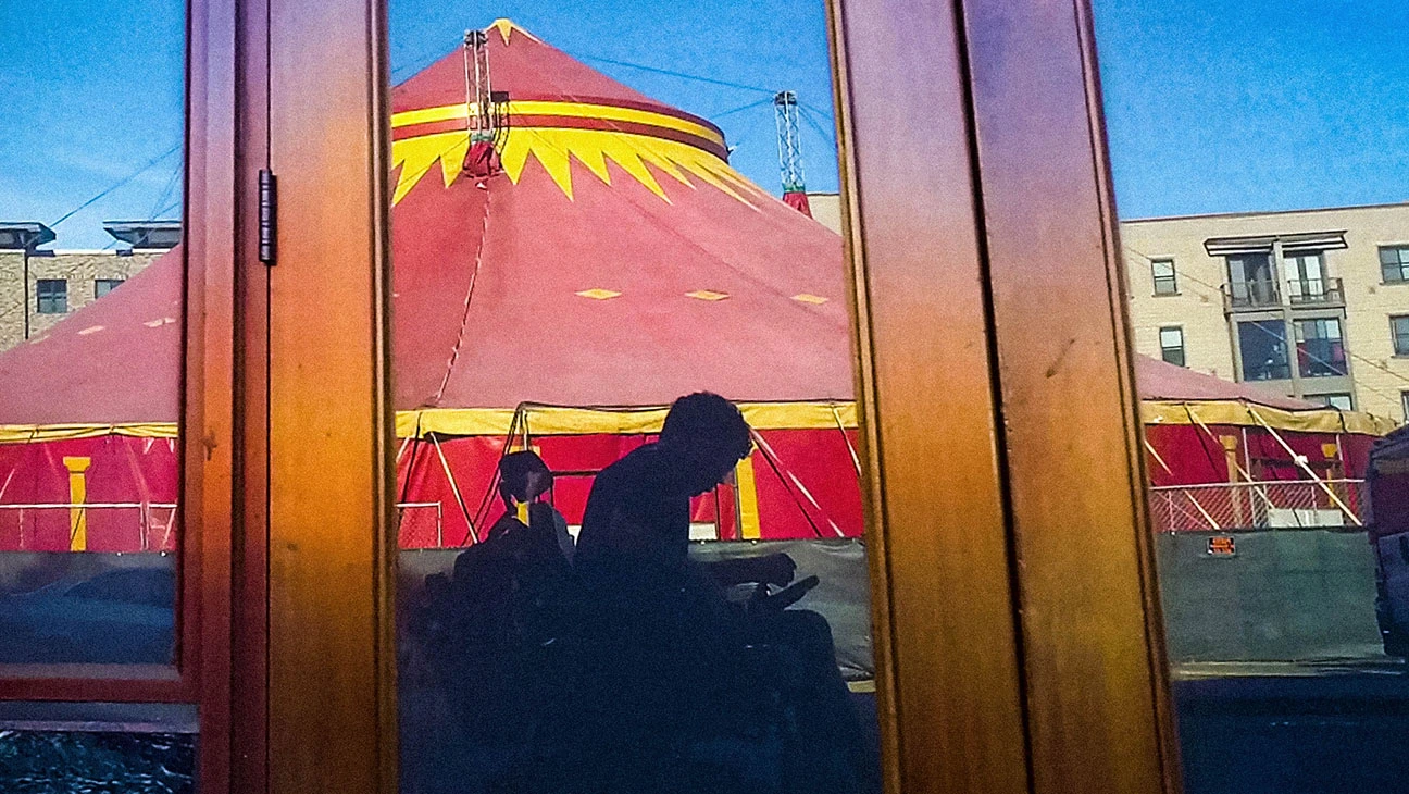 A man in a motorized wheelchair silhouetted in front of a circus carousel