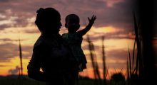 A woman and her baby silhouetted against magic hour sky