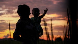 A woman and her baby silhouetted against magic hour sky