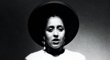 A black-and-white photo of a Black woman in a white shirt and black wide-brimmed hat
