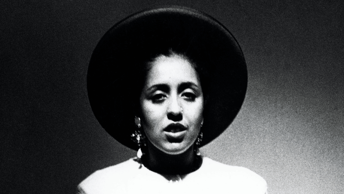 A black-and-white photo of a Black woman in a white shirt and black wide-brimmed hat