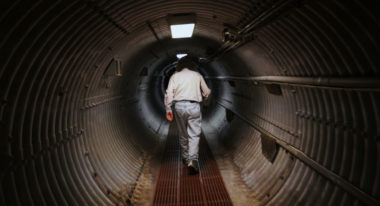 A man walking down a long tunnel into an underground bunker