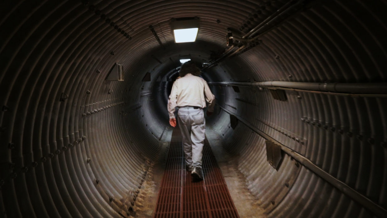 A man walking down a long tunnel into an underground bunker
