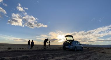 A hatchback car in the desert and three people shooting a movie