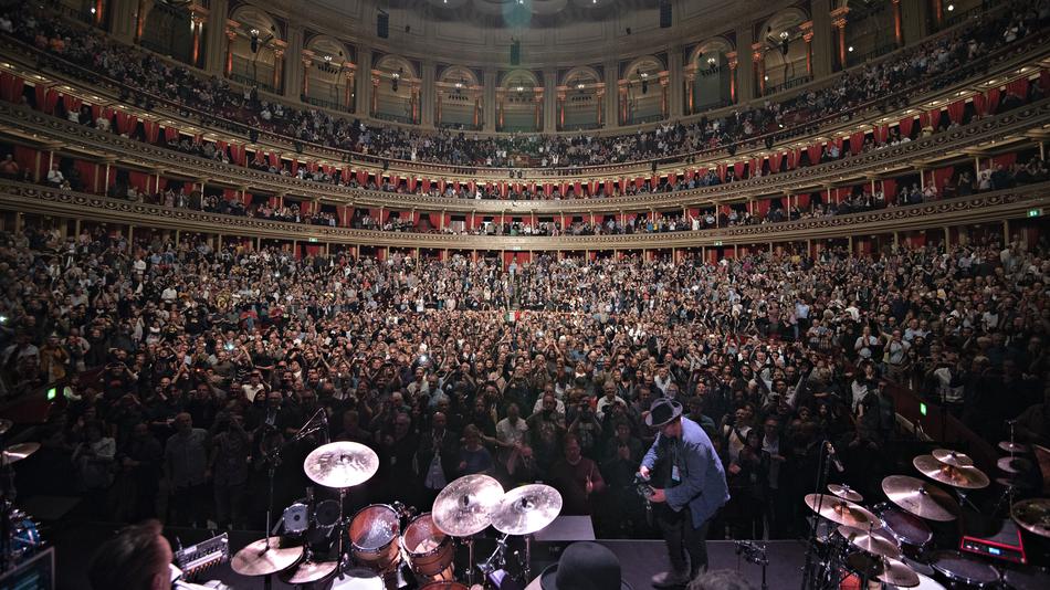 A drummer on stage at a giant concern hall filled with listeners