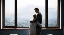 A father and daughter hugging in front of a window overlooking a city