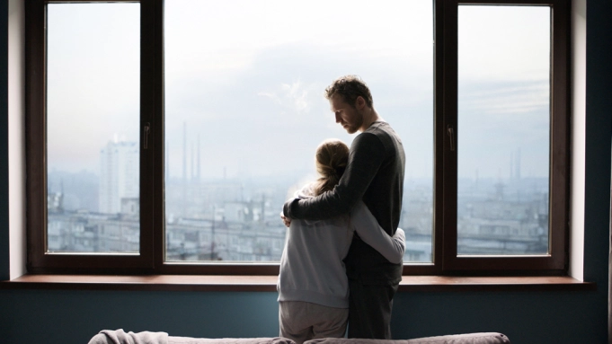 A father and daughter hugging in front of a window overlooking a city