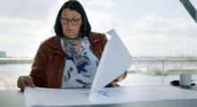 A middle-aged woman with brown hair wearing a red jacket looking at papers in a scene from the documentary "Undercurrent: The Disappearance of Kim Wall"