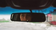 A woman's face (Lily Gladstone) seen through the mirror in a moving car