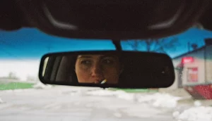 A woman's face (Lily Gladstone) seen through the mirror in a moving car