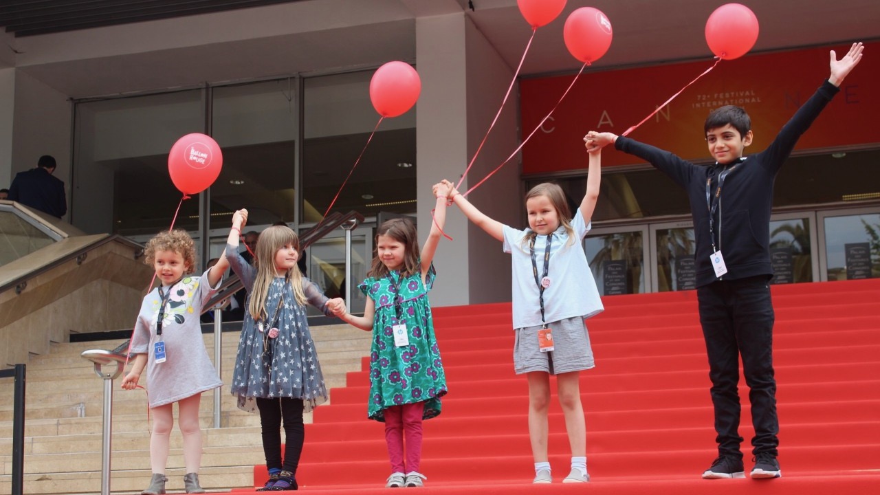 Four children holding balloons on the red carpet of the Cannes Film Festival