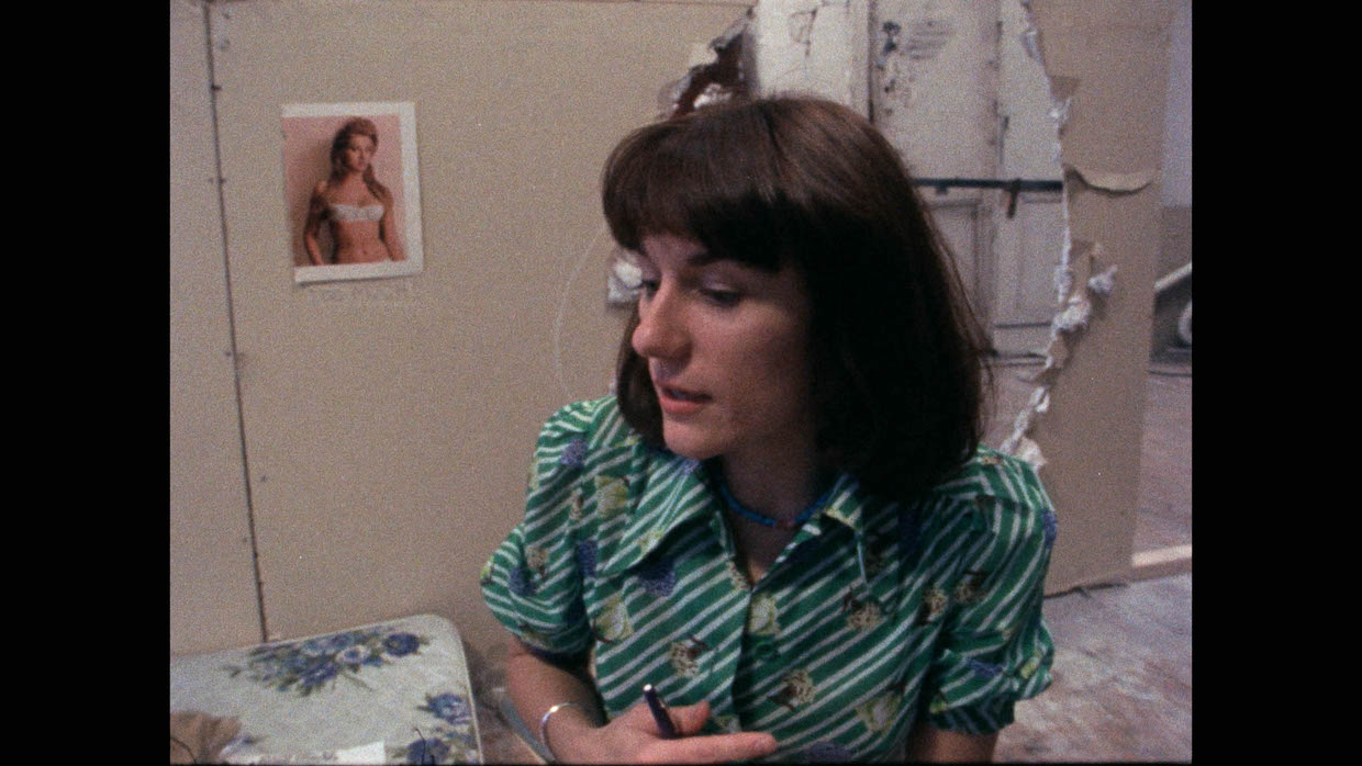A middle-aged woman with brown hair and a green top in a room with beige walls