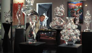 Detective Benoit Blanc (Daniel Craig) stands in a room surrounded by glass figurines on black pedestals.