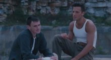 Two young white men sit next to each other on a rocky embankment, the man on the left is played by Jeremy Davies and has dirty blond hair, a white t-shirt and open green button up shirt. He also has bandages on his hands. The man on the left is played by Ben Affleck, who is clean-shaven and sporting a slick brown hairstyle. He wears a white tank top and green cargo pants with a brown belt.