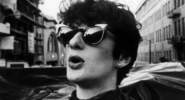 A black-and-white photo of 20-ish woman with short black hair and sunglasses on a city street.