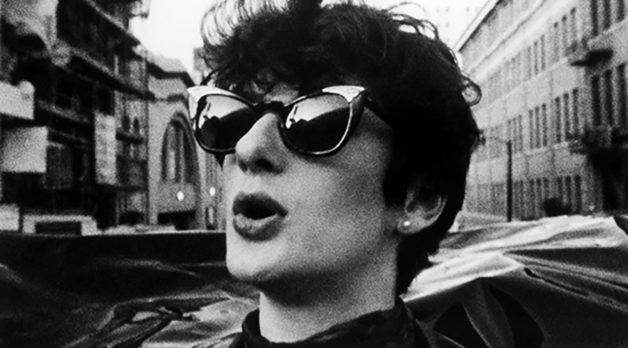 A black-and-white photo of 20-ish woman with short black hair and sunglasses on a city street.