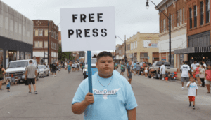 A young man wearing a blue t-shirt holds a sign that reads "free press."