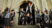 Children wearing school uniforms dance, leap and cheer on the steps leading into their boarding school.