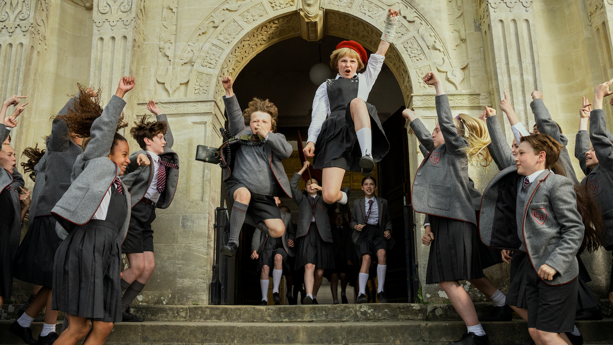 Children wearing school uniforms dance, leap and cheer on the steps leading into their boarding school.