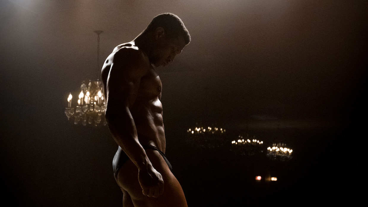 A body builder's full-body profile can be seen accentuated by dim lighting.