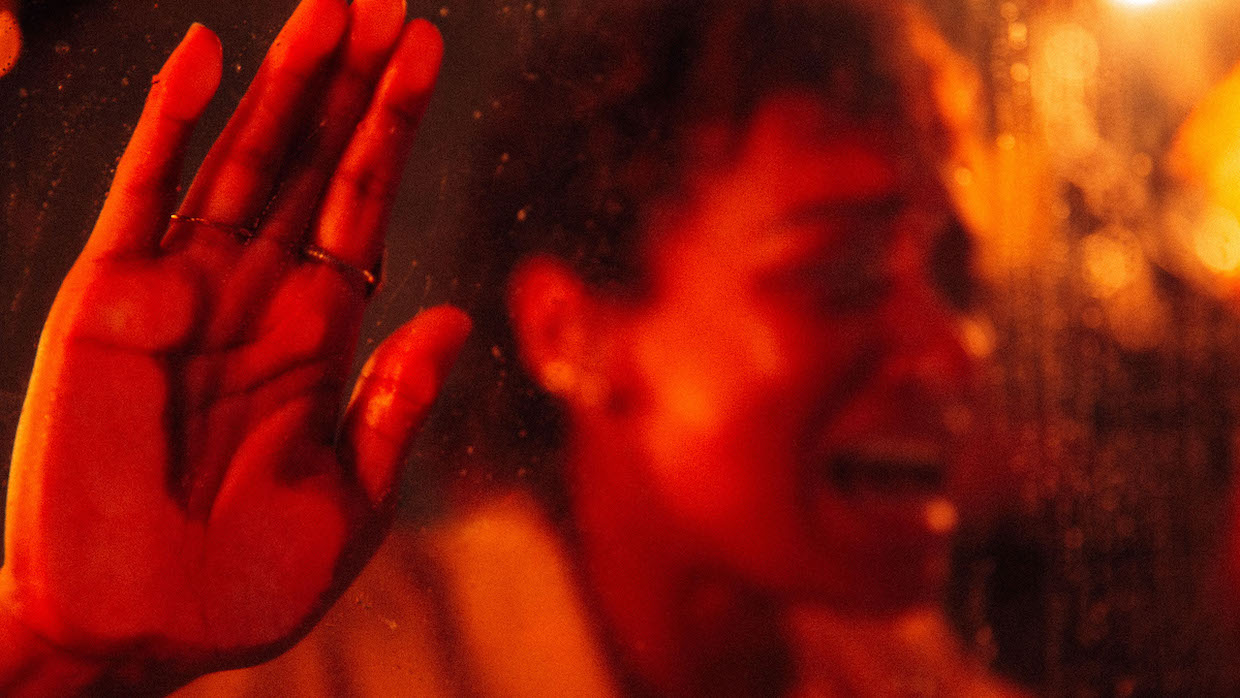 A woman screams with her hand pressed against a window. She is bathed in deep red light.