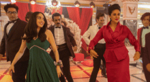 An Iranian-American family lines up on a dance floor. A mother and daughter stand in front of male relatives wearing tuxedos. The younger woman wears a green gown while the mother wears a red suit skirt ensemble.