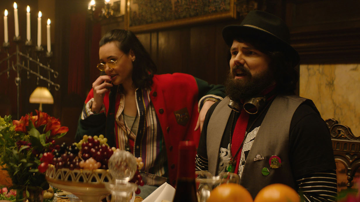 A man and a woman wearing antiquated garb sit at a table in front of a feast.