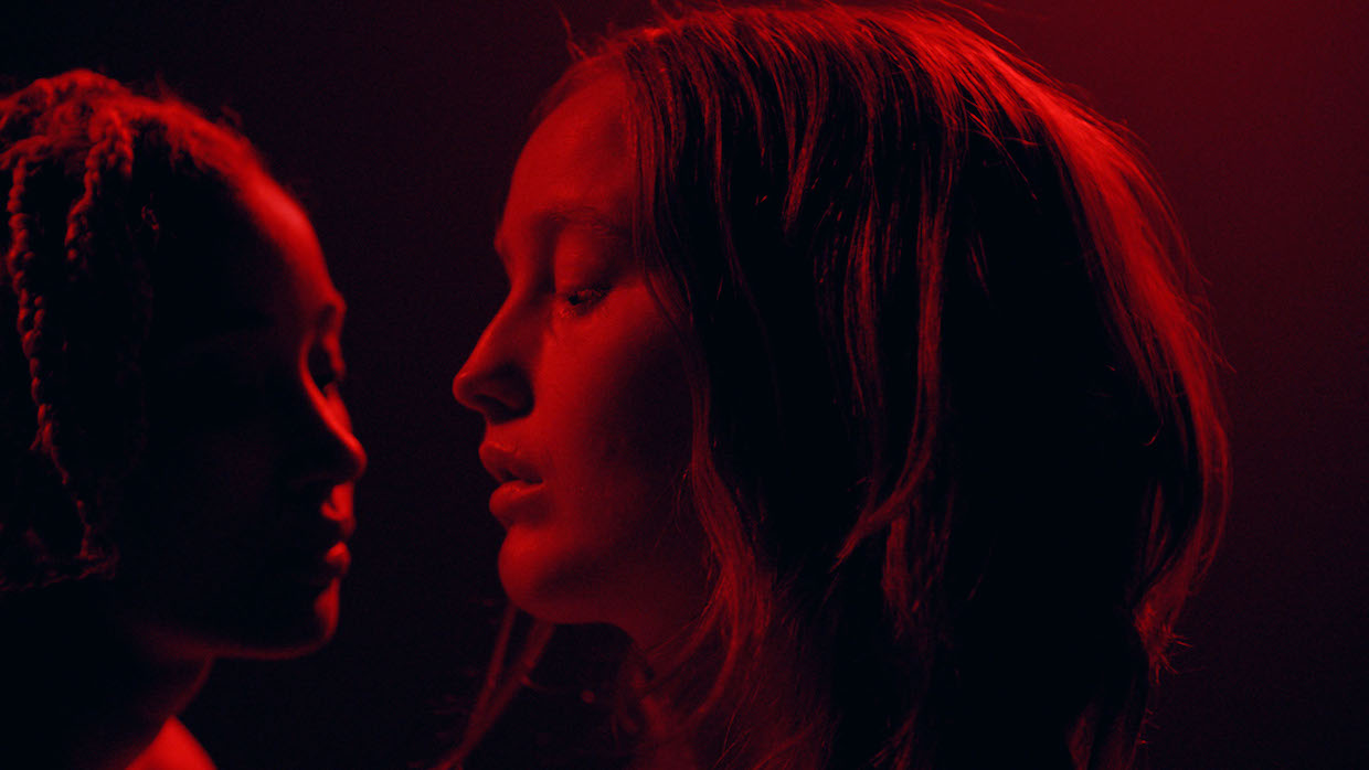 Two girls stand with their faces inches apart, completed drenched in red light.