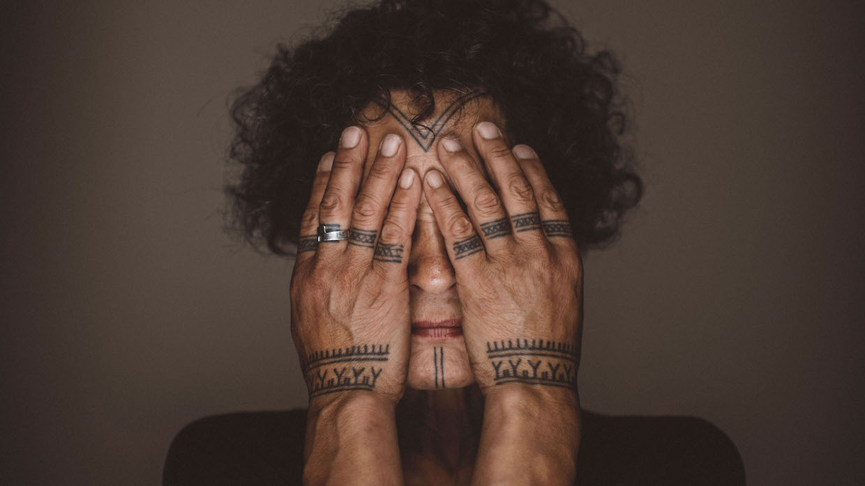 Aaju Peter covers her eyes and shows off her Indigenous hand tattoos in the documentary Twice Colonized.