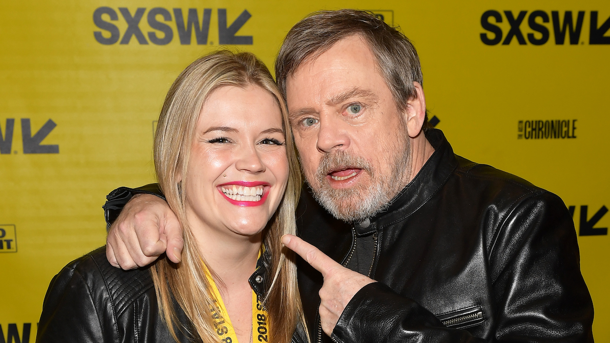 Claudette Godfrey, a young woman with straight, blond hair and red lipstick, poses with actor Mark Hamill, who has salt and pepper hair and a beard.