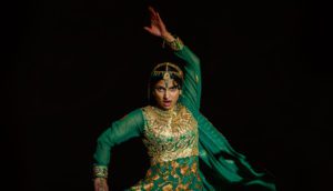 A teenage girl in traditional, green Desi formal wear strikes a pose as she performs a traditional dance.