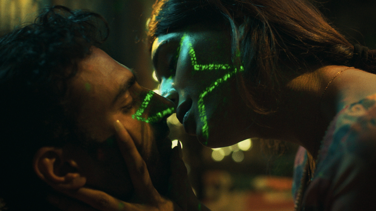 A woman holds a man's face in her hands as she leans in for a kiss. A green star in projected over her side profile.