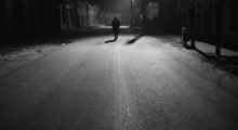 A black and white shot of a man walking down a vast, desolate street.