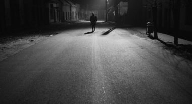 A black and white shot of a man walking down a vast, desolate street.