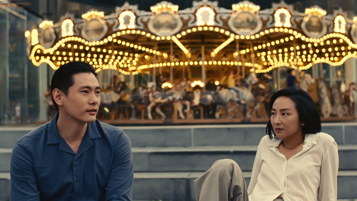 Two 30-something Koreans, a man and a woman, sit in front of a carousel.