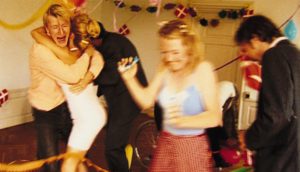 A handful of young, predominantly blonde young Danish people dance at a party.