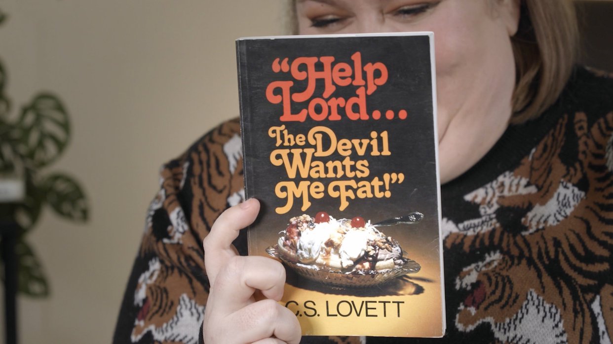 Fact activist Aubrey Gordon holds up a book called Hello Lord...The Devil Wants Me Fat!" in Jeanie Finlay's Your Fat Friend