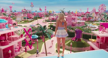 The character of Barbie is seen from the back as she stands looking out at the pink buildings in Barbie's world.