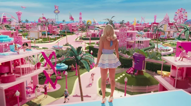 The character of Barbie is seen from the back as she stands looking out at the pink buildings in Barbie's world.