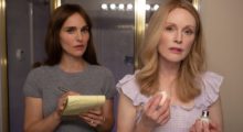 Natalie Portman wears a gray t-shirt and hold a yellow legal pad. She takes notes while Julianne Moore, wearing a pink, ruffle-sleeved garment, does her make-up in a bathroom mirror.