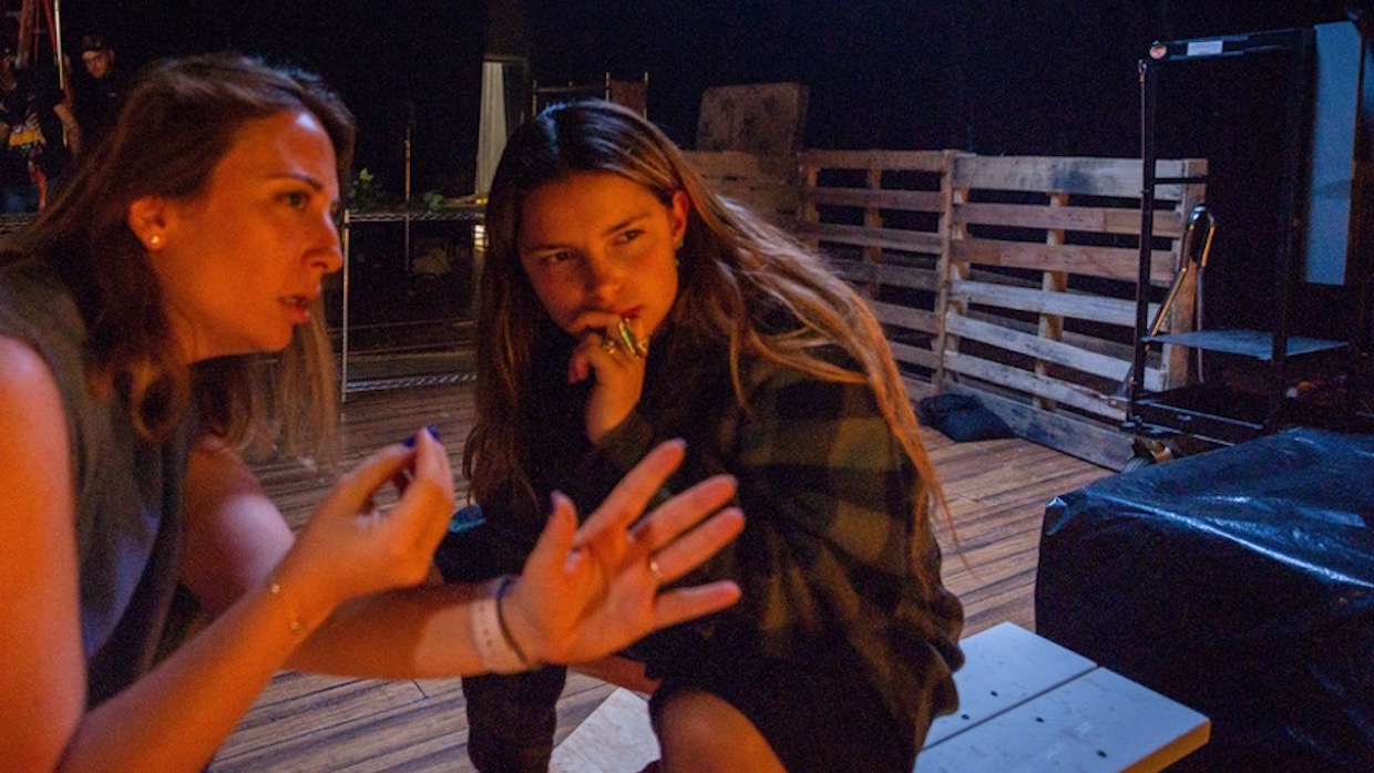 Two young women with brown hair kneeling on a porch at night.