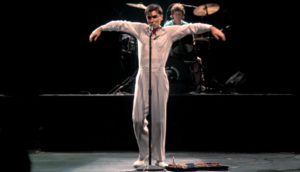 Talking Heads frontman David Byrne extends his arms and sings into the microphone circa 1983.