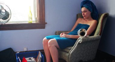 A woman sits in a chair wrapped in a blue bath towel with a matching one wrapped around her head.