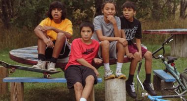 Four Native American kids sit at/on a table with their bikes nearby.