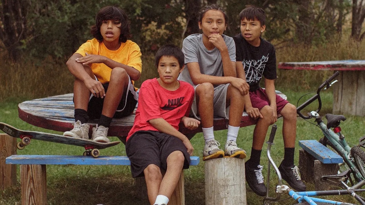 Four Native American kids sit at/on a table with their bikes nearby.