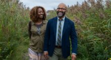 A smiling Black woman (played by Erika Alexander) and Black man (Jeffrey Wright) hold hands in a field.