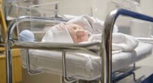 A baby lies in a cradle in a hospital room.