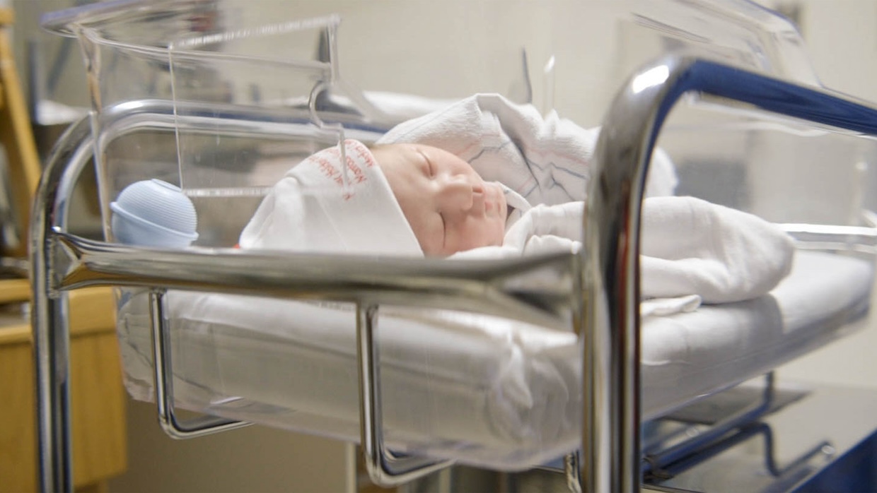 A baby lies in a cradle in a hospital room.