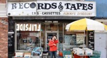 A man clutches his forehead standing beneath the awning of a record store.
